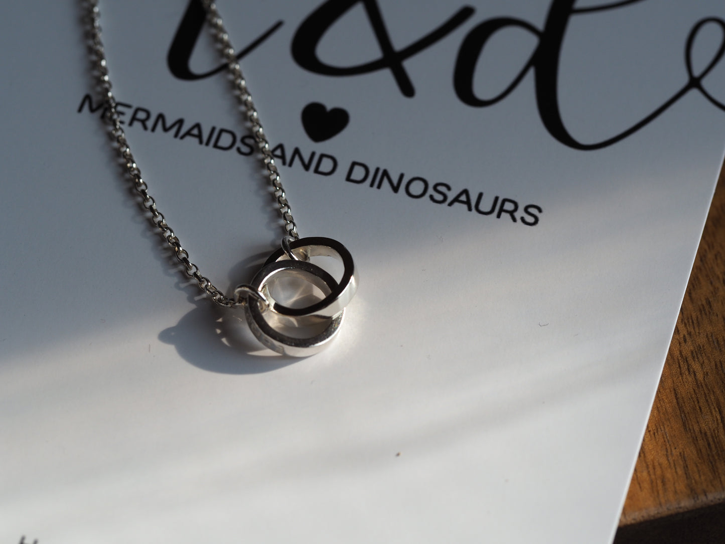 side view of silver interlinked ring necklace on a mermaids and dinosaurs card