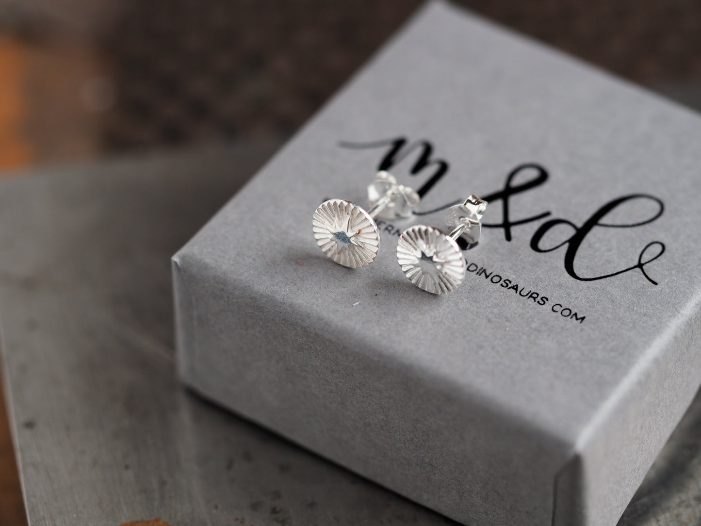 Silver stud earrings on a gray box with 'm&d' branding.
