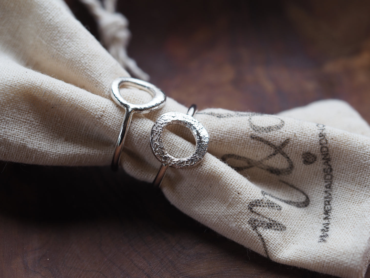 A sterling silver ring with a molten circle face placed on a beige fabric with a printed design.