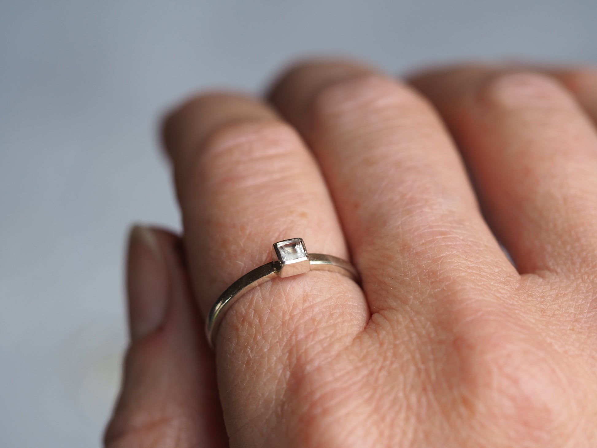 A sterling silver square cubic zirconia ring on a finger.