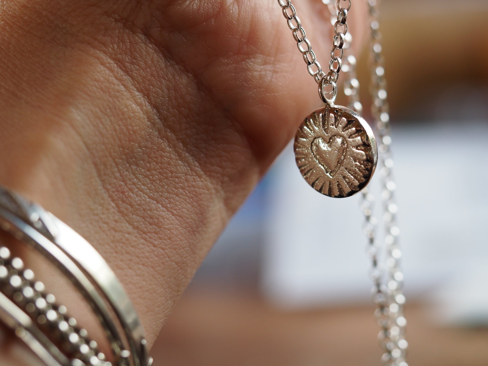 Close-up of a hand holding a silver ring and a necklace with a heart pendant.