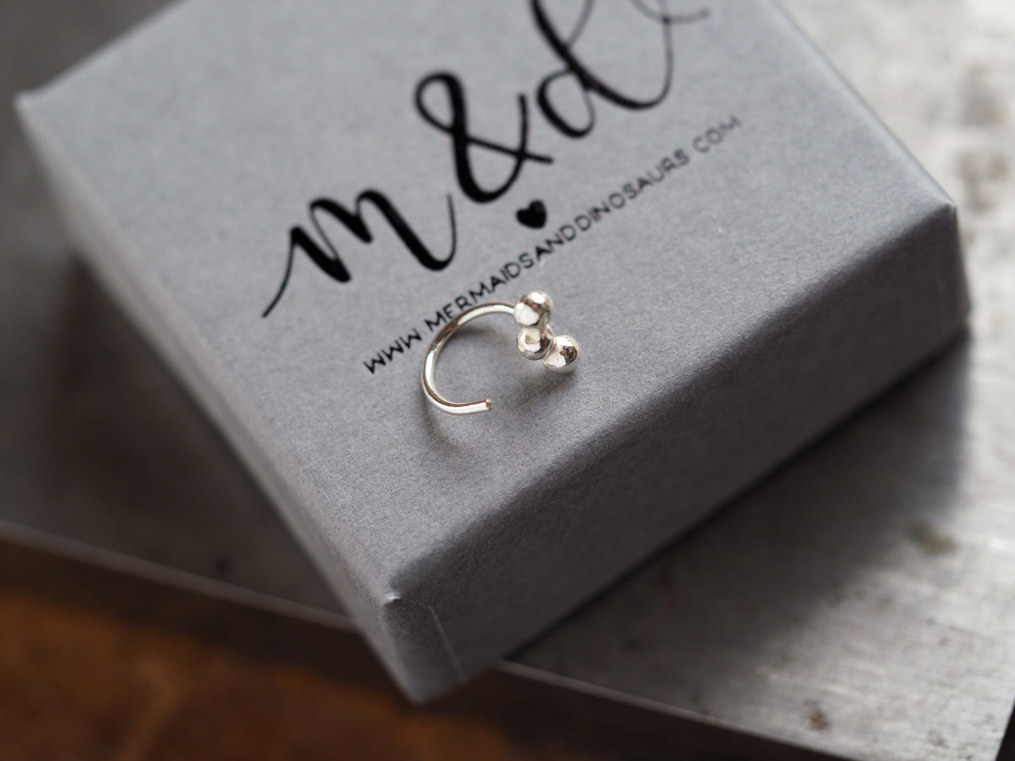 Silver earring on a gray jewelry box with 'm&d' branding.