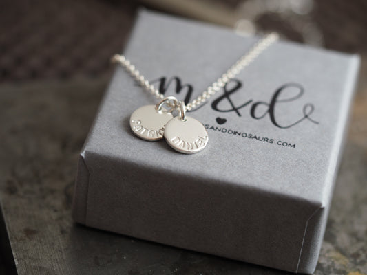 Silver necklace with two round pendants on a gray box with 'm & d' branding.
