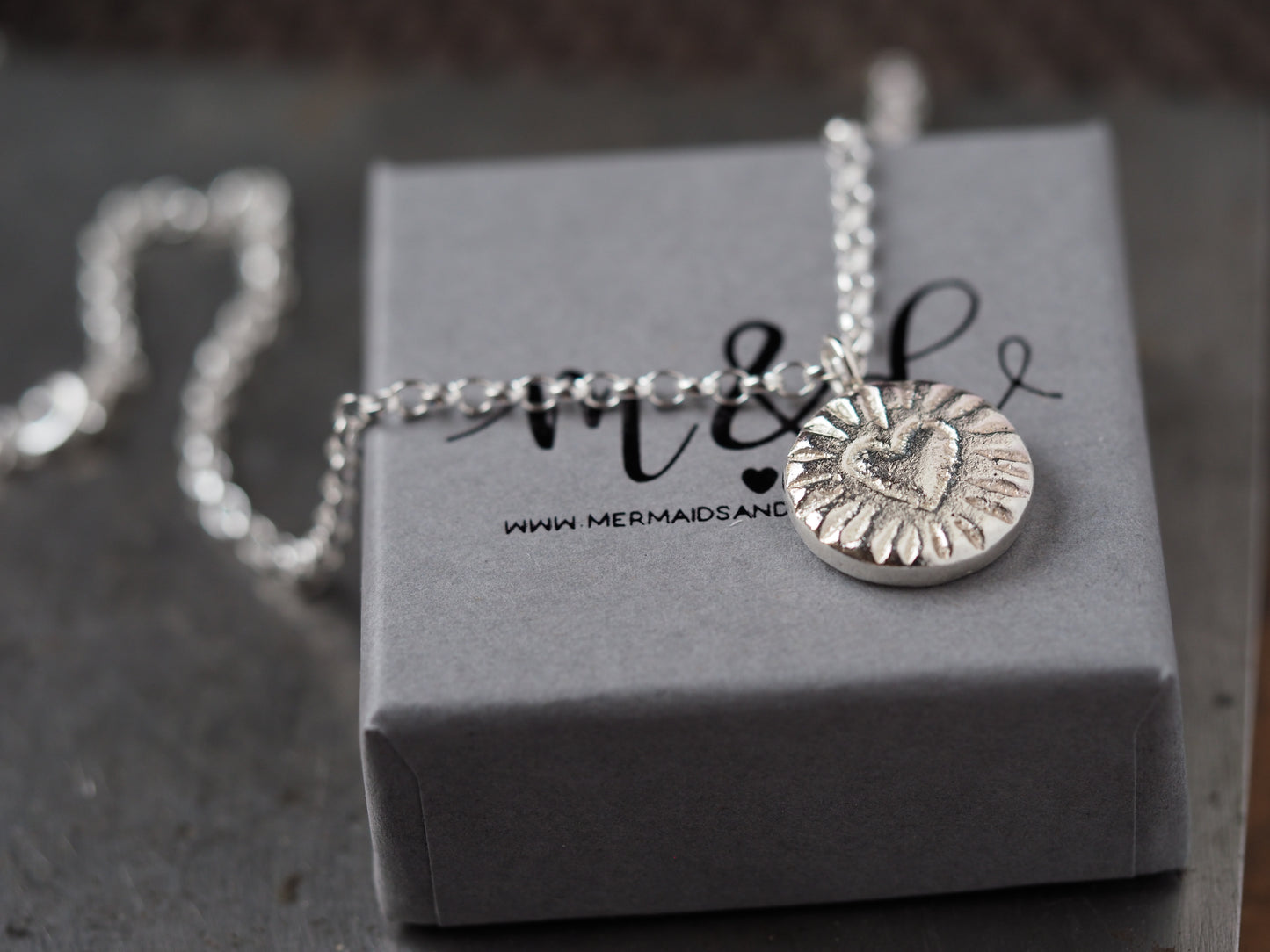 Silver necklace with a heart pendant on a grey box with 'Mermaids & Dinosaurs' branding.