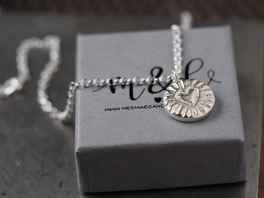 Silver necklace with a heart pendant on a grey box with 'Mermaids & Dinosaurs' branding.