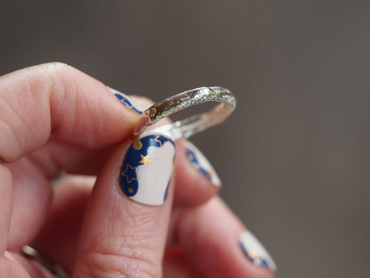 Silver ring held between fingers with decorative nail polish on a blurred background