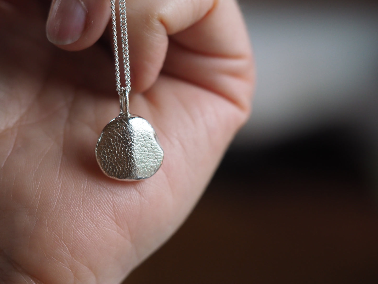 Silver pendant necklace held in a hand with a blurred background
