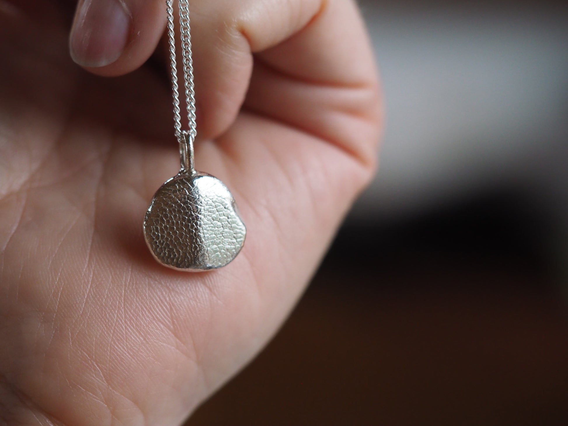 Silver pendant necklace held in a hand with a blurred background