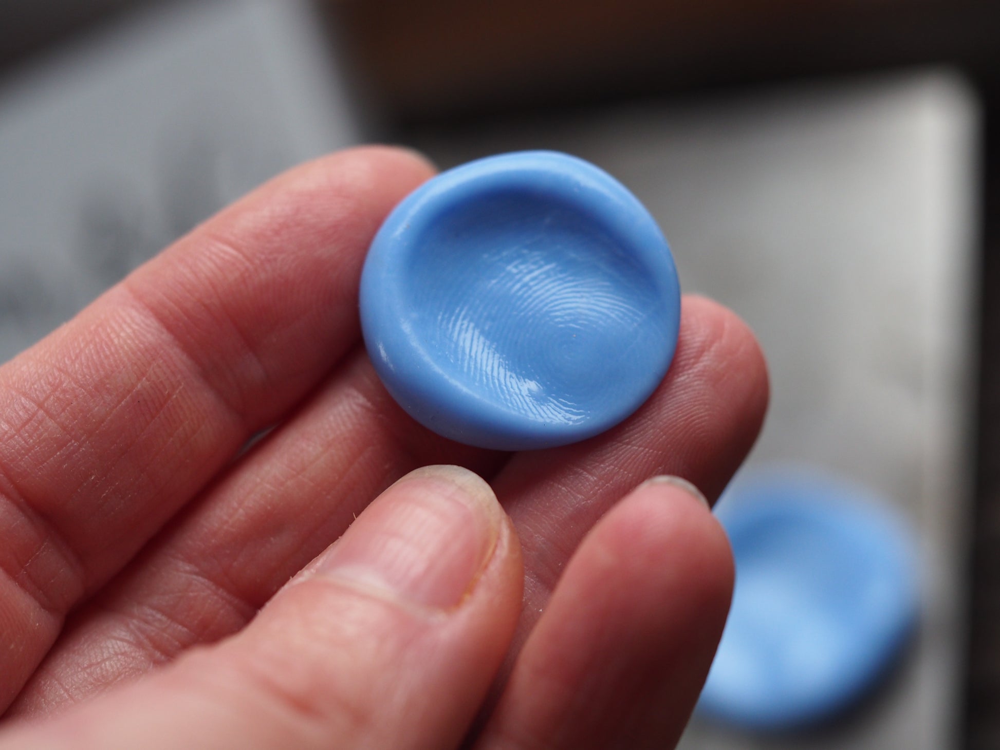 Blue fingerprint mould held in a hand with a blurred background