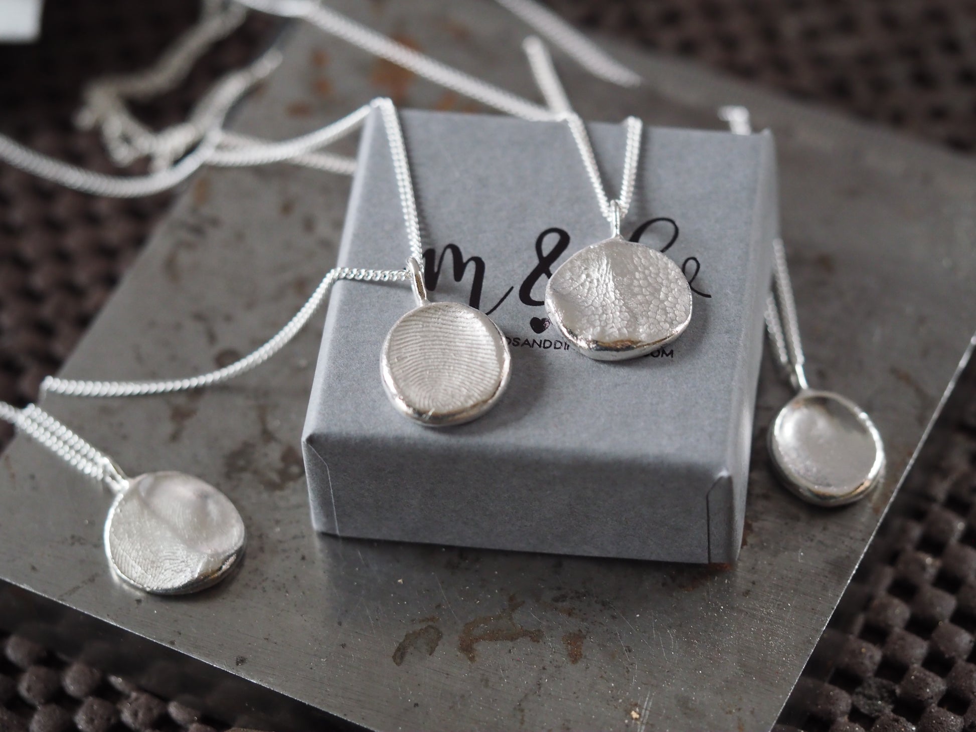 Silver necklace and earrings on a gray jewelry box with 'm & d' branding.