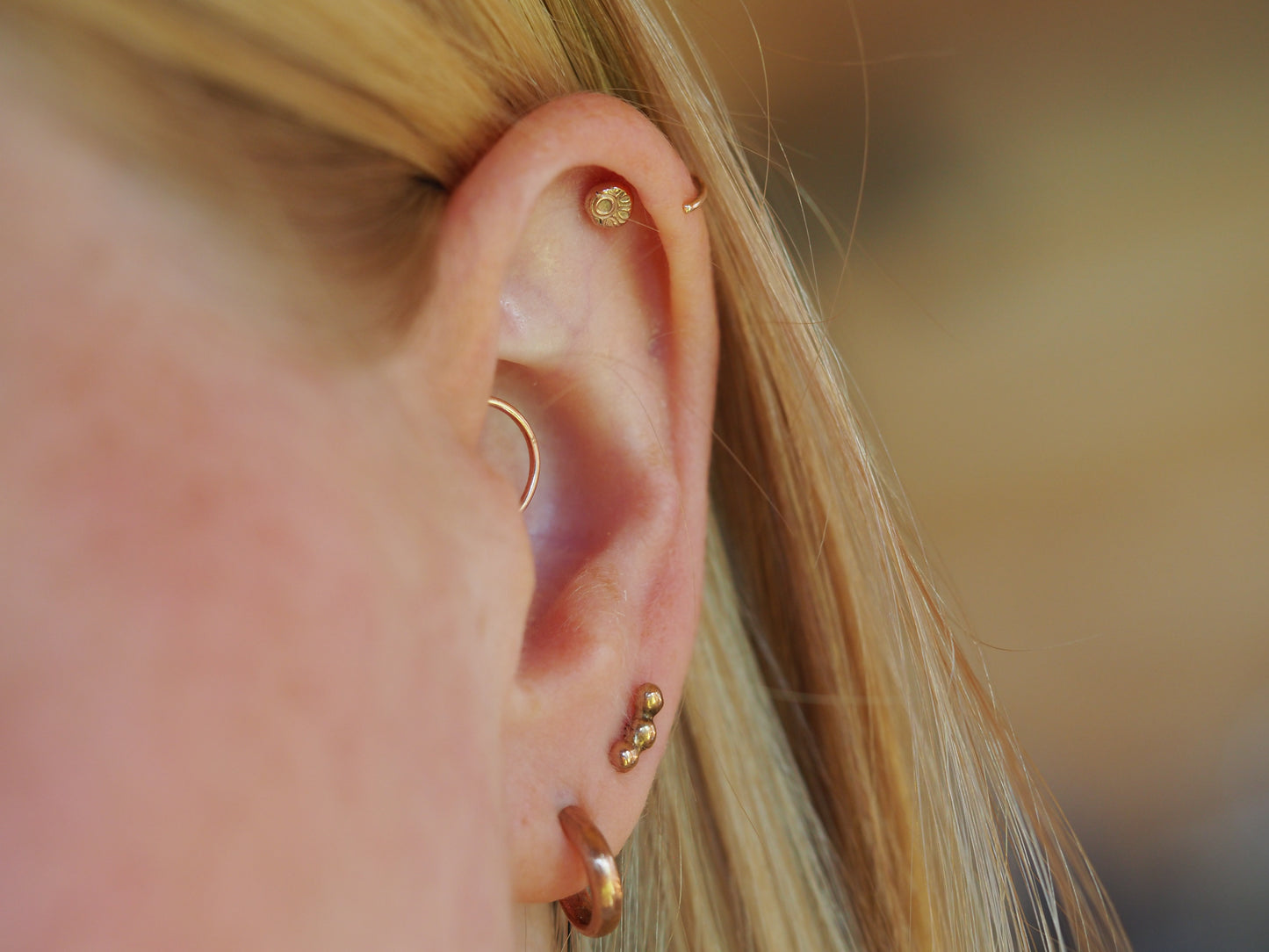 Close-up of an ear with gold earrings against a blurred background