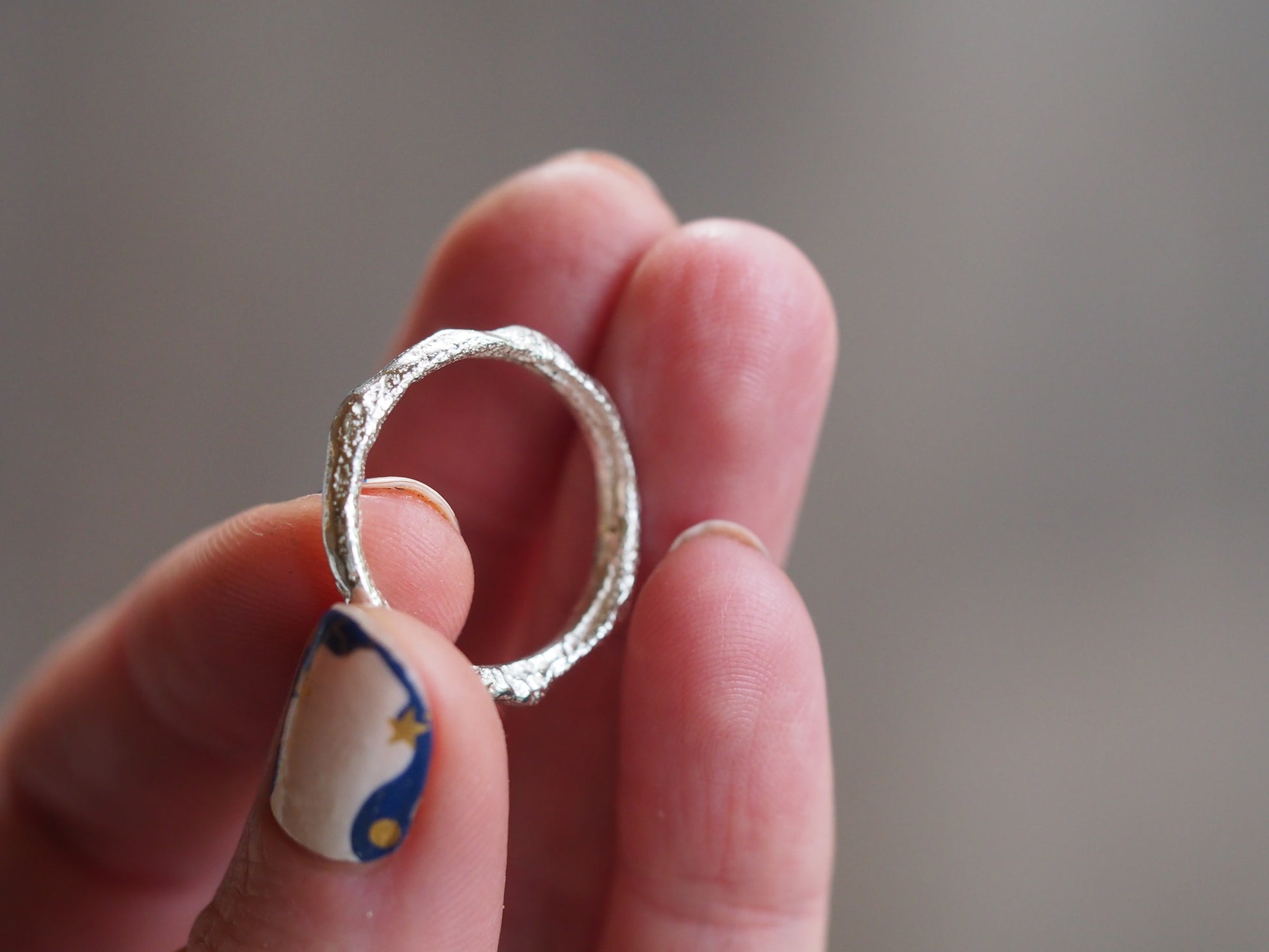 Hand holding a silver ring with a blurred background