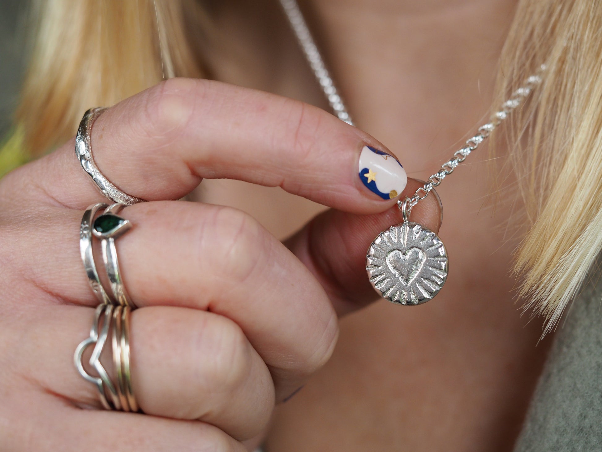 Close-up of a hand wearing multiple rings with a silver necklace featuring a heart pendant.