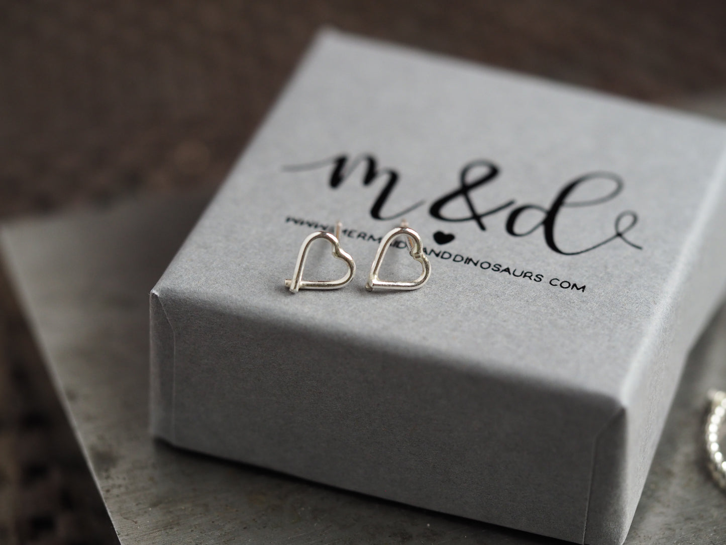 Heart-shaped earrings on a gray box with 'm&d' branding.
