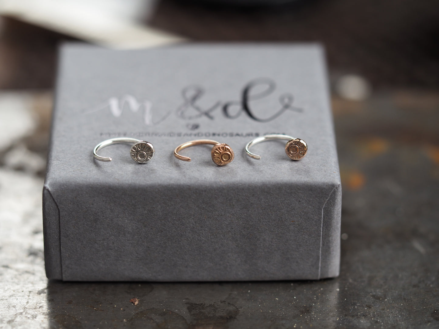 Three small helix earrings on a grey box with 'M&D' branding.