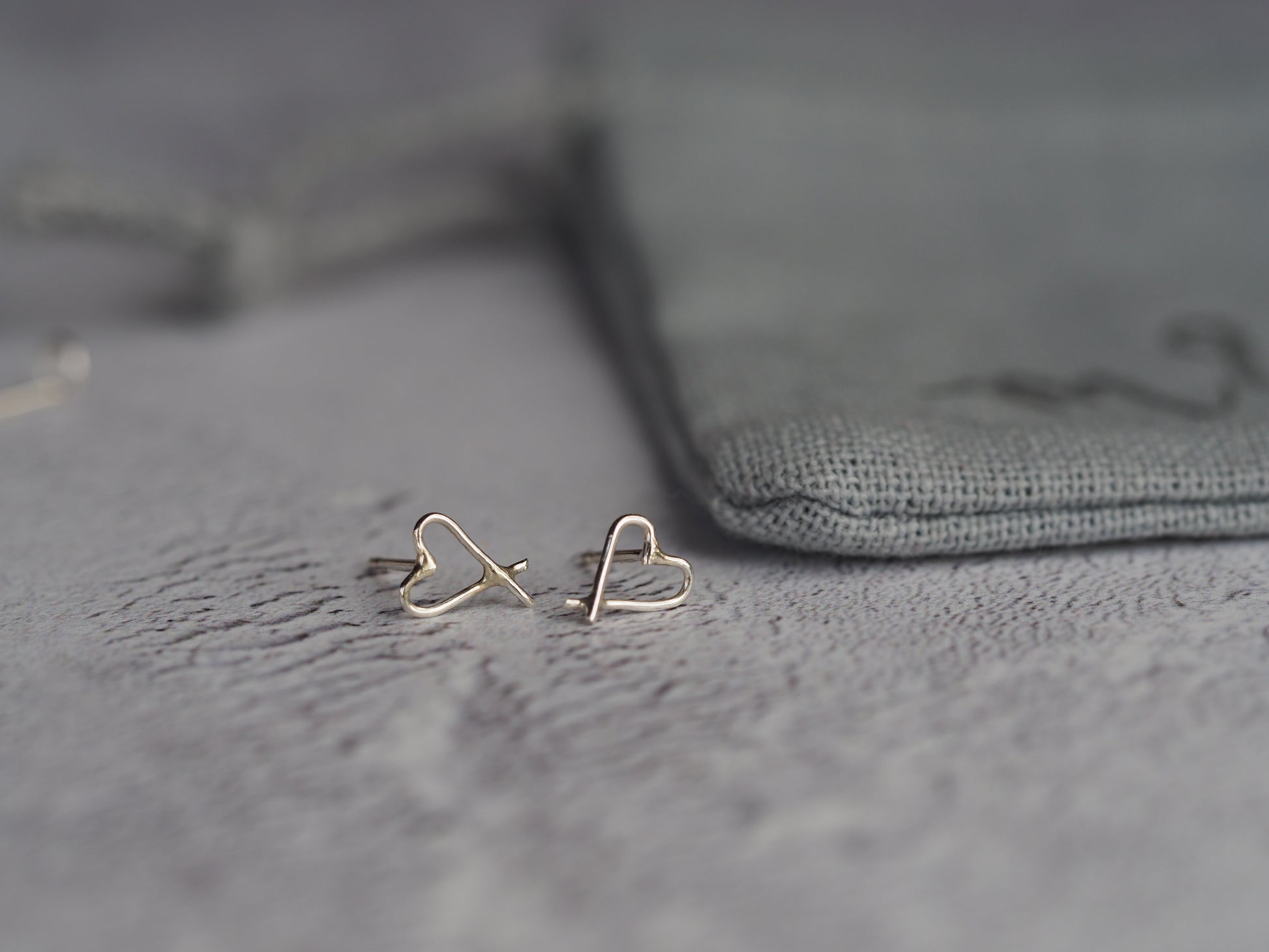 A pair of sterling silver open heart earrings with roll butterfly backs, placed on a textured surface.