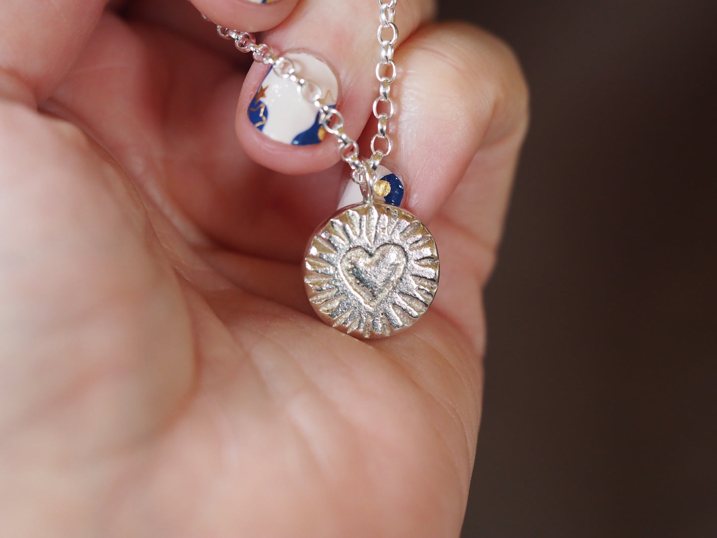 Silver necklace with a heart pendant held in a hand against a blurred background