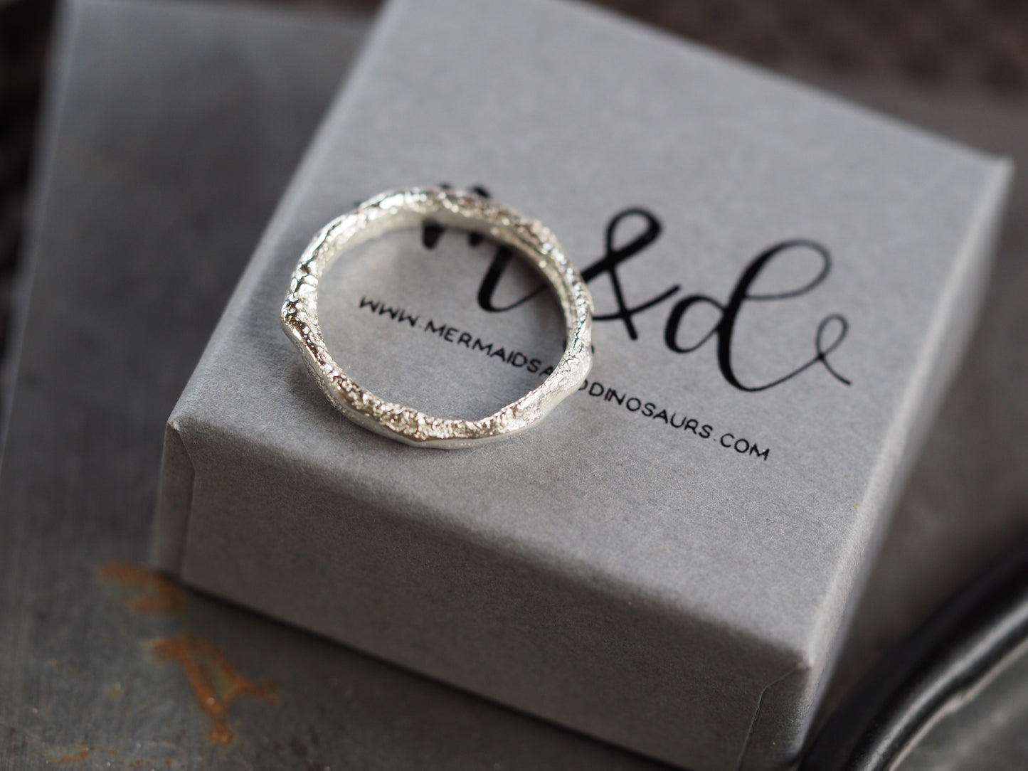 Silver ring on a gray box with 'mermaids & dinosaurs' branding