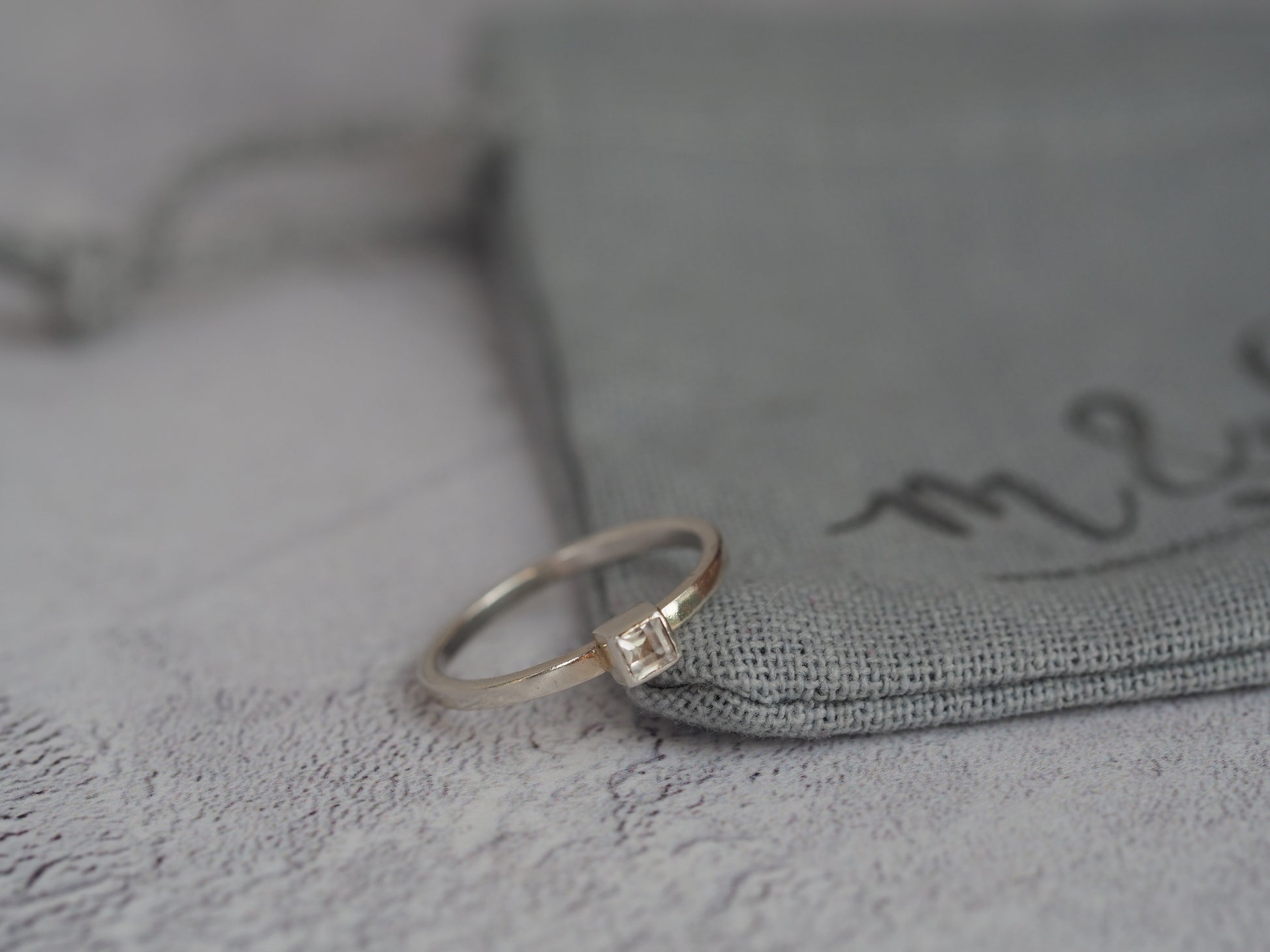 silver square cubic zirconia ring sat on a grey cotton gift bag