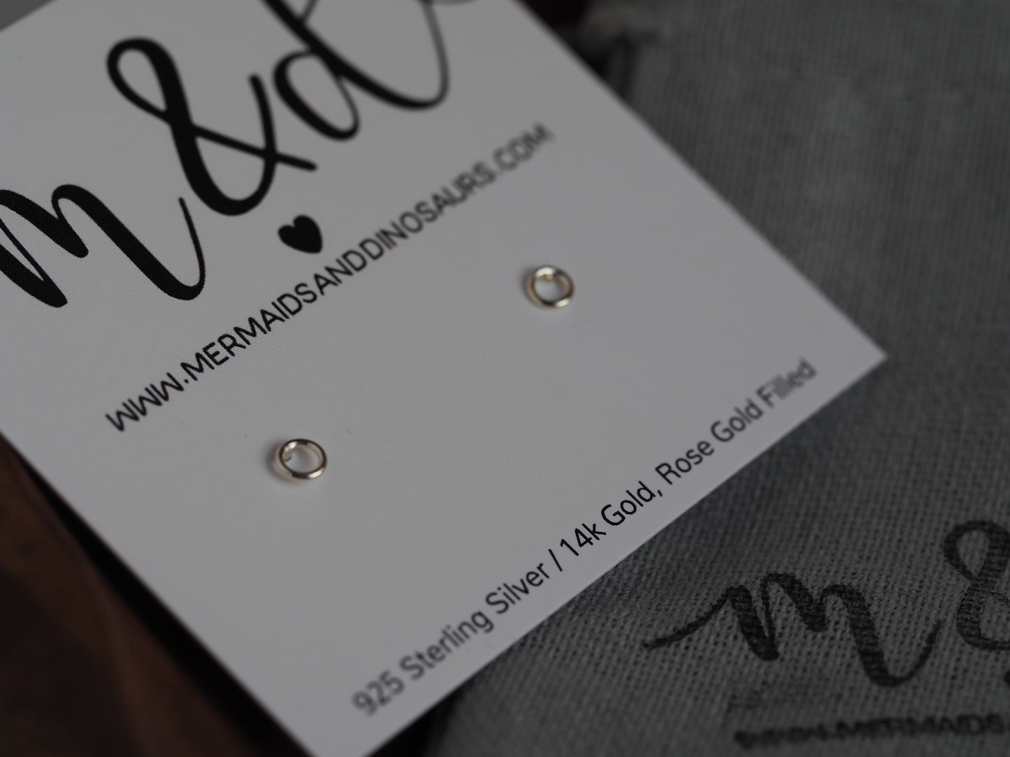 A pair of sterling silver circle earrings with roll butterfly backs, displayed on a white card with 'M&D' and 'Mermaids and Dinosaurs' branding.