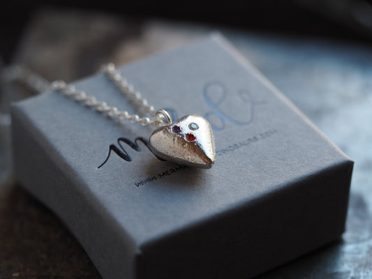 A solid silver heart birthstone necklace with multiple cubic zirconia stones set in the heart shape, displayed on a grey box with the brand 'M&D'