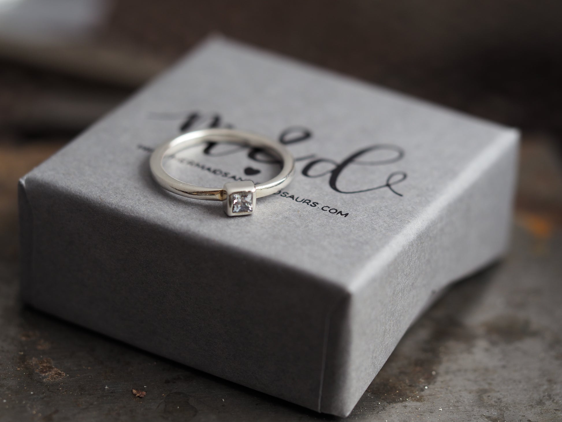 silver ring with a square cubic zirconia on a gray box 
