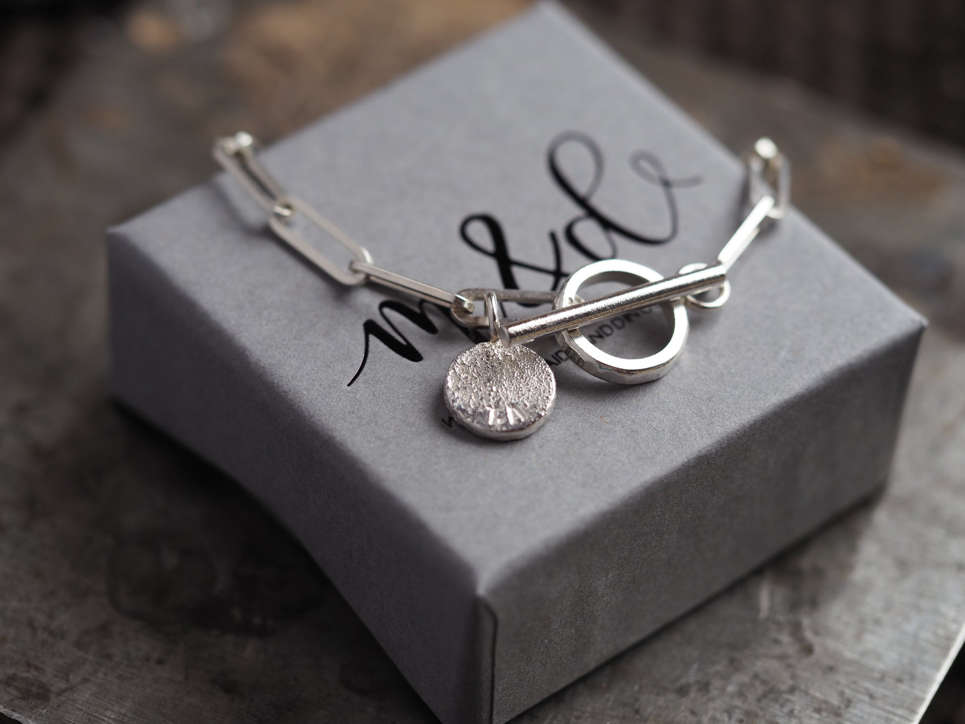 Silver paperclip chain with a single charm on a grey box with 'm&d' branding.