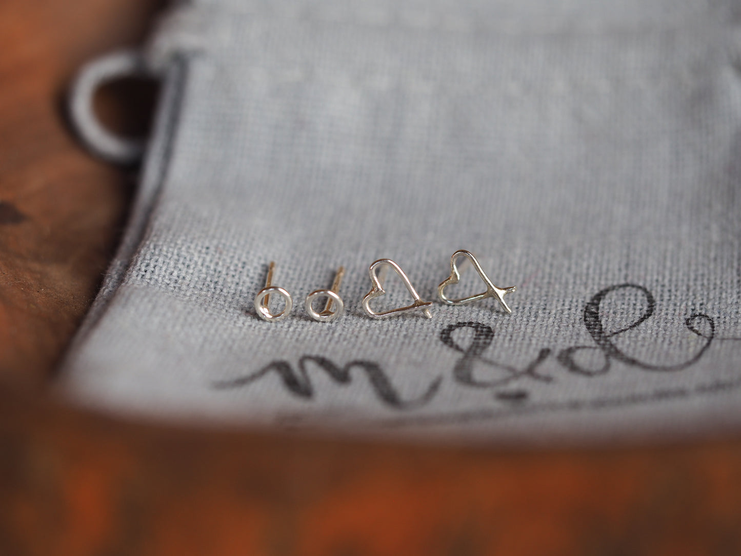 sterling silver circle and heart stud earrings on a grey cotton M&D branded bag