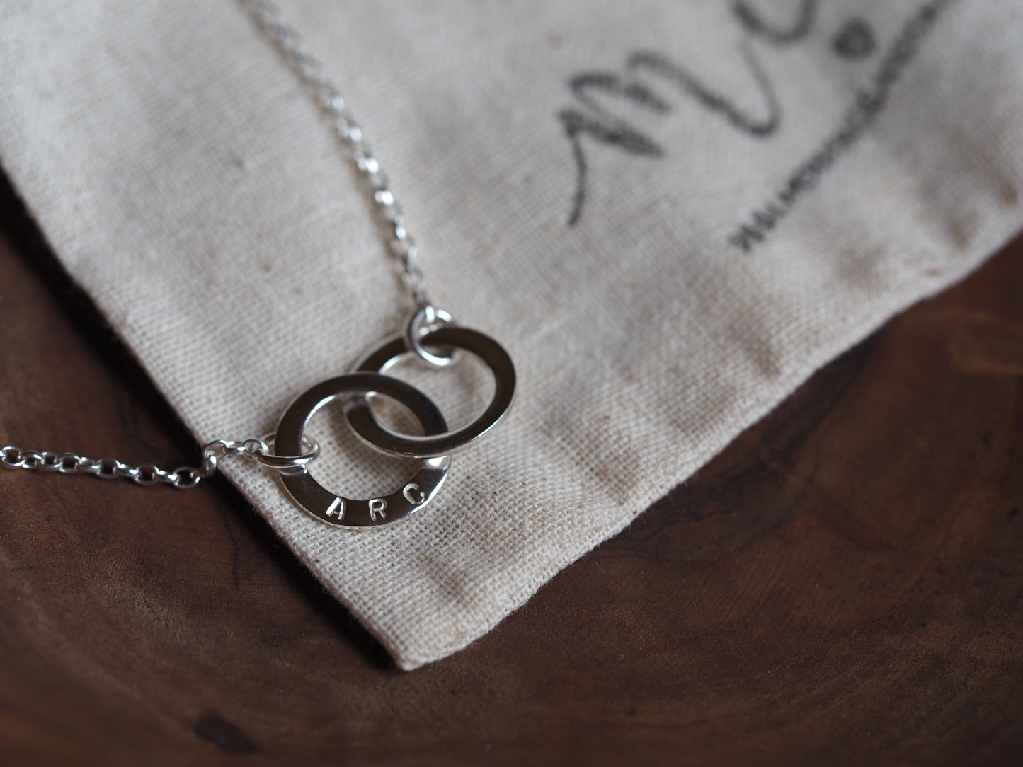A silver interlinked mini washer necklace laid out on a beige fabric pouch.
