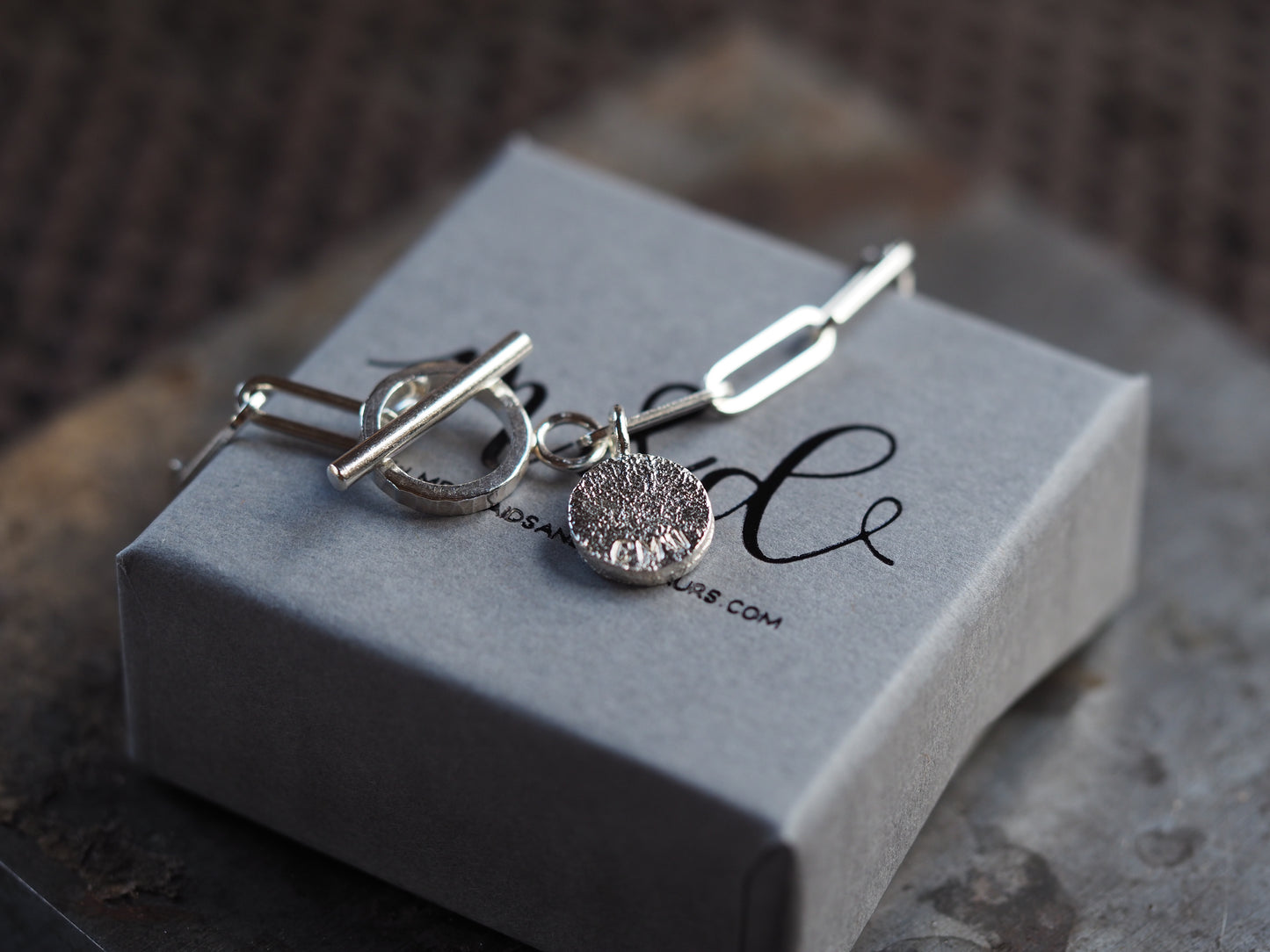 Silver paperclip chain with a single charm on a grey box with 'm&d' branding.