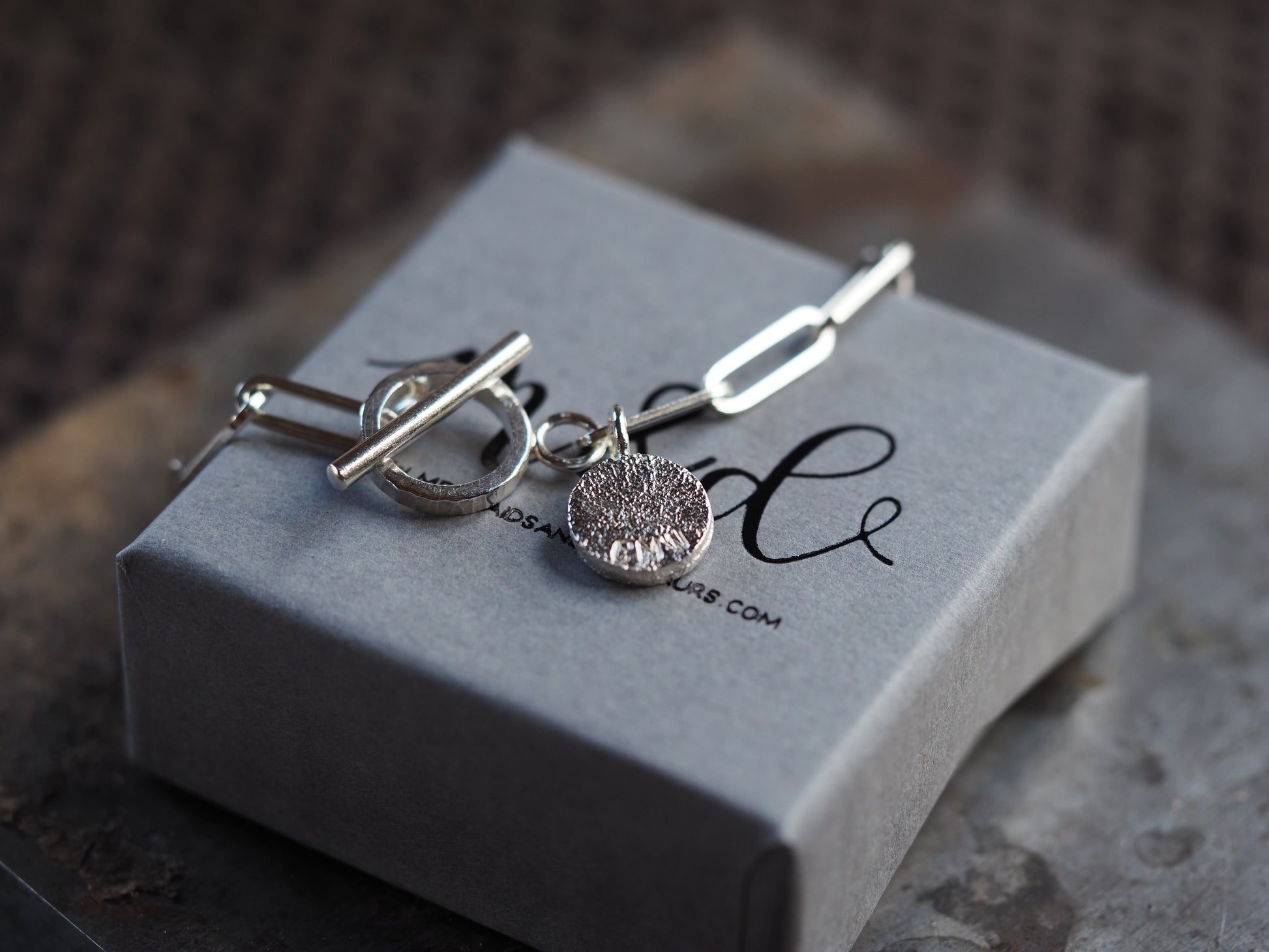 Silver paperclip chain with a single charm on a grey box with 'm&d' branding.