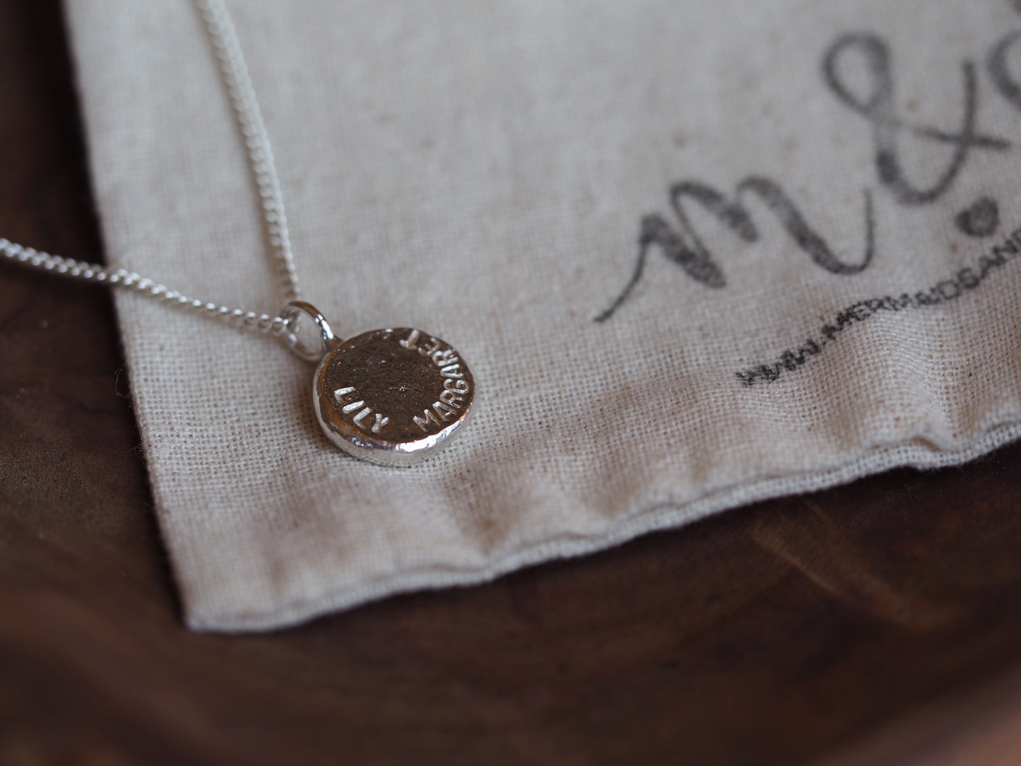 A sterling silver nugget necklace laid out on a beige fabric with the brand mark visible, showcasing the polished yet rugged texture of the metal.