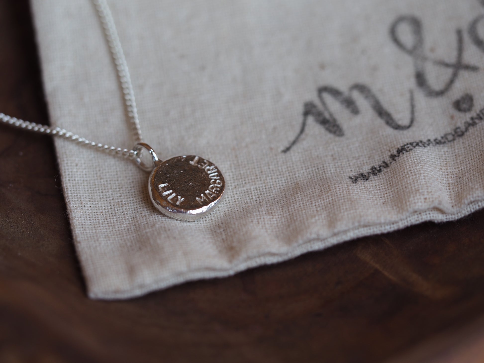 A sterling silver nugget necklace laid out on a beige fabric with the brand mark visible, showcasing the polished yet rugged texture of the metal.