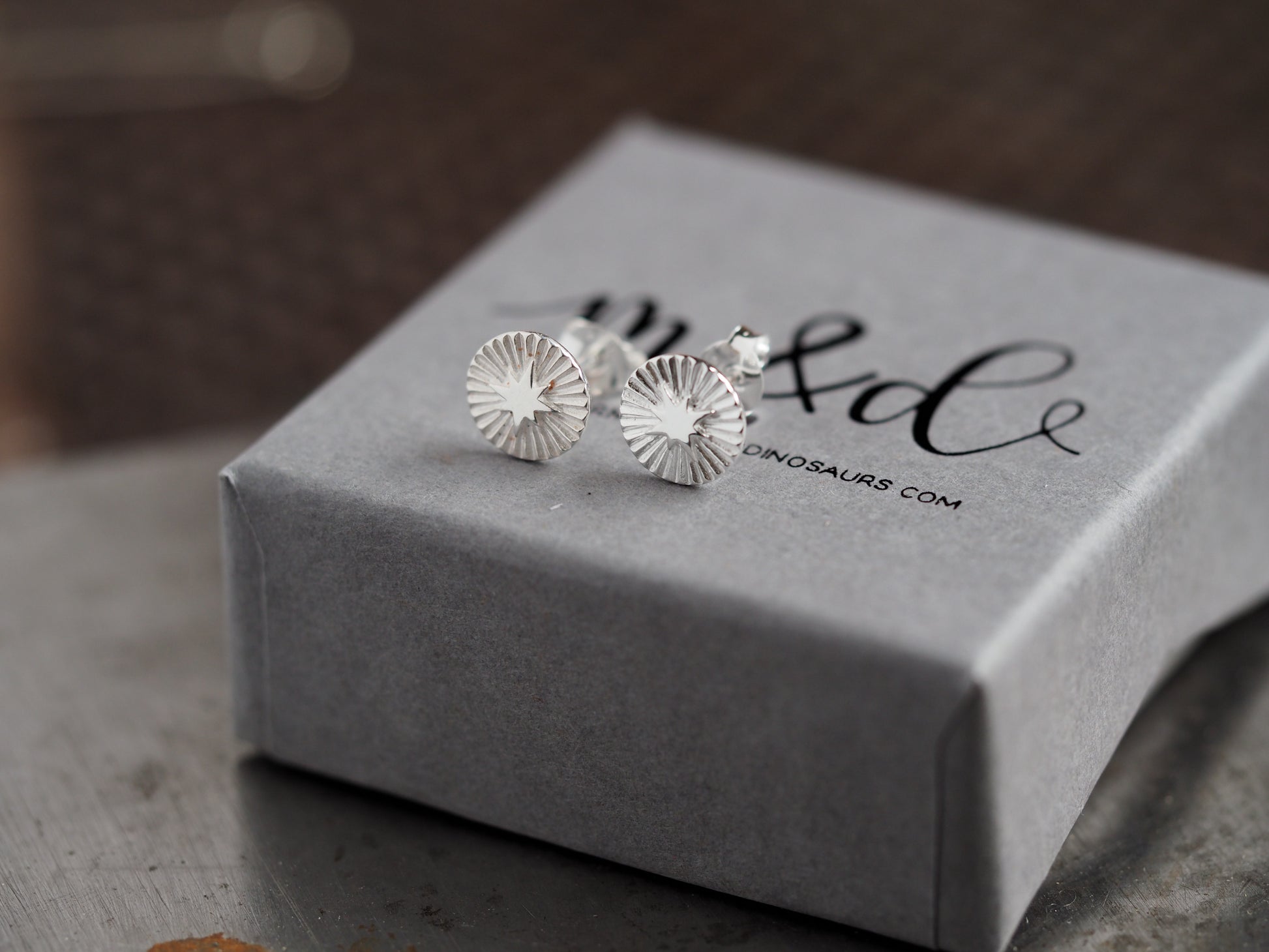 Silver earrings on a gray box with 'm&d' branding.